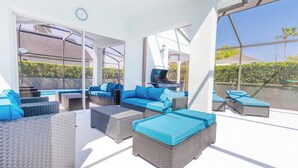 A sunlit outdoor lounge area with wicker furniture and a television.