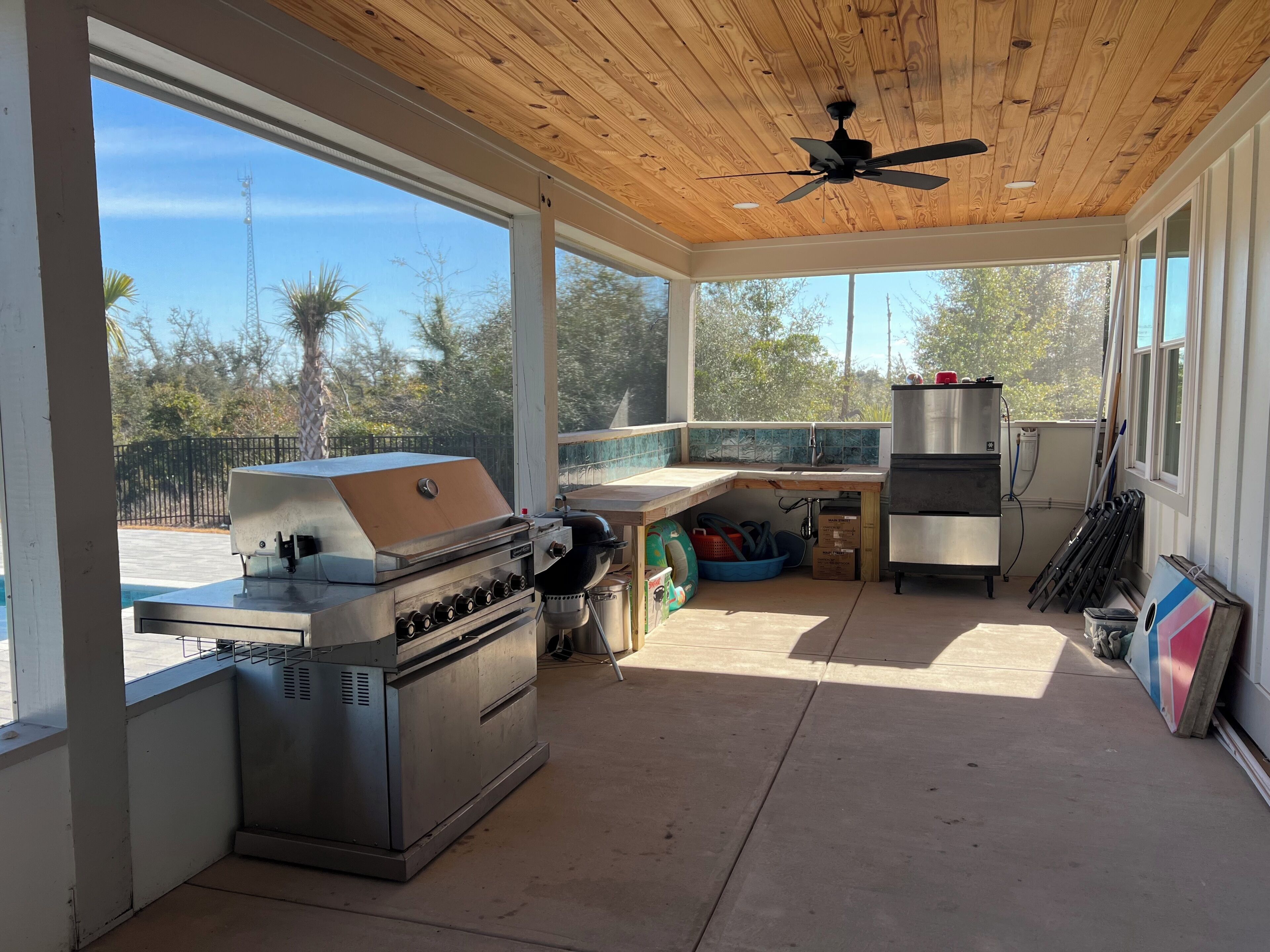 A covered outdoor kitchen with a grill, a sink, and a ceiling fan.