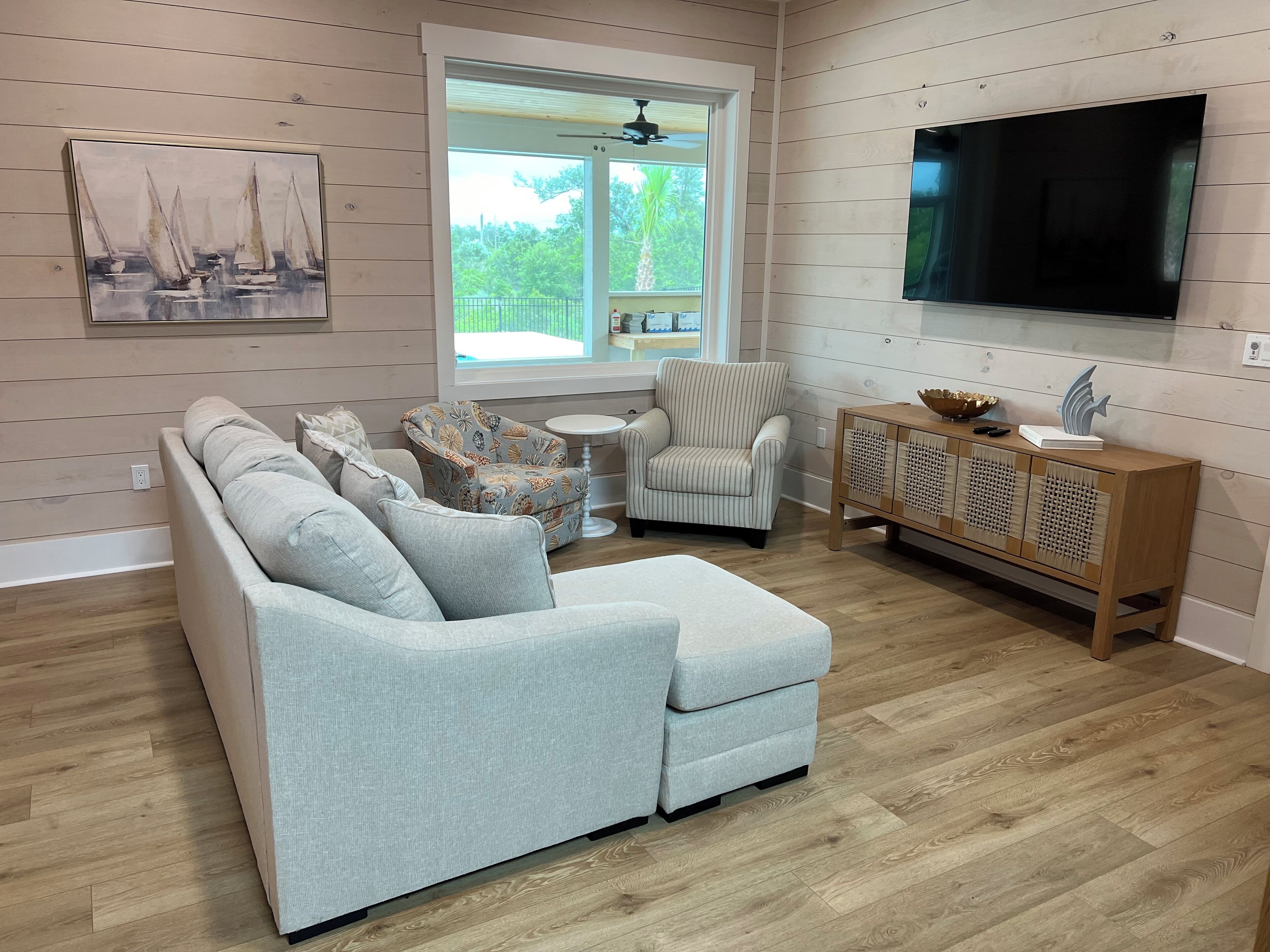 Un salon moderne avec un canapé d’angle, un fauteuil à rayures, une petite table ronde et un meuble en bois sur lequel est fixé un téléviseur au mur.