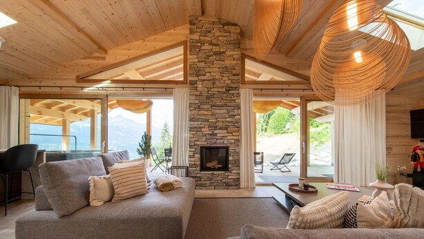 A cozy living room with a stone fireplace, wooden ceiling beams, and large windows offering a mountain view. - Chalet Eteila Combloux proche Megève (Combloux)
