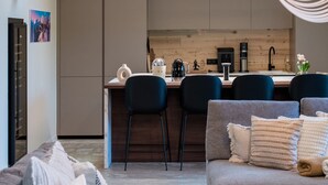 A modern living room with a grey sofa, a coffee table, and a dining area with a kitchen in the background. - Chalet Eteila Combloux proche Megève (Combloux)