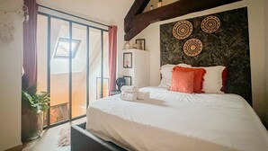 A bedroom with a large bed, a window with curtains, a ceiling fan, and a wall with decorative items. - Casa Jungle loft rue du Paquier (Annecy)