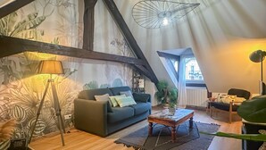 A cozy loft-style living room with a high ceiling, exposed wooden beams, a large window, a hanging light fixture, a sofa, a coffee table, and a floor lamp. - Casa Jungle loft rue du Paquier (Annecy)