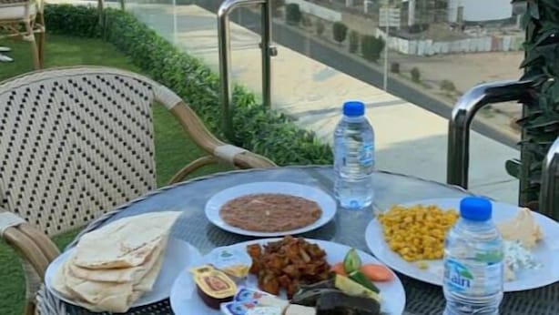 A balcony with a table set with food, a water bottle, and a chair. - Zekra Alkawther Hotel (Taif)