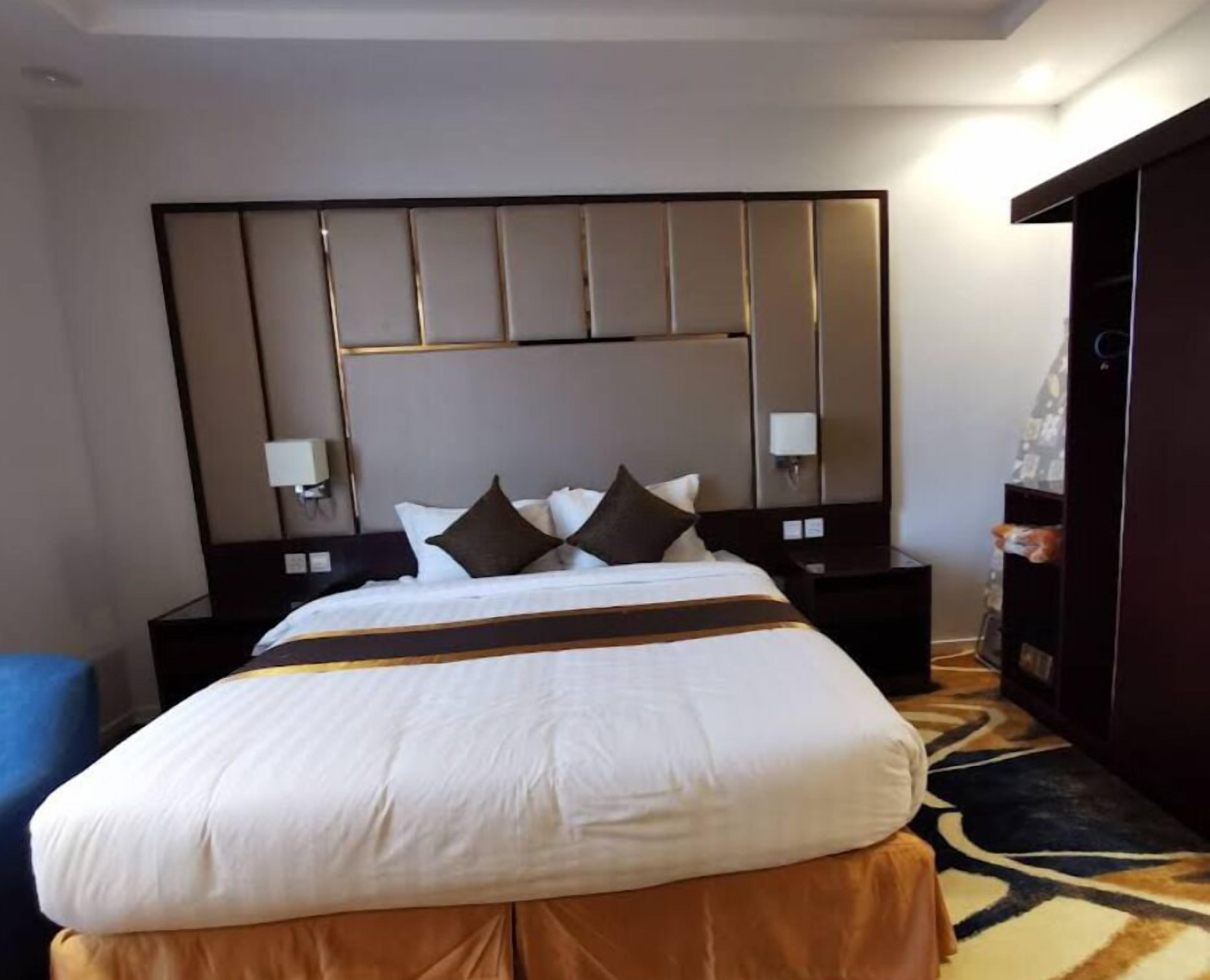 A hotel room with a large bed, a headboard with vertical panels, two bedside tables with lamps, and a patterned carpet.
