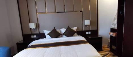 A hotel room with a large bed, a headboard with vertical panels, two bedside tables with lamps, and a patterned carpet.