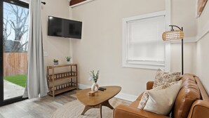 A living room with a brown leather sofa, a wooden coffee table, a TV mounted on the wall, and a floor lamp.
