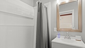 A bathroom with a shower curtain, a sink with a mirror, and a toilet.