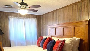 Un dormitorio con cabecera de madera, cama con ropa de cama blanca y ventilador de techo.