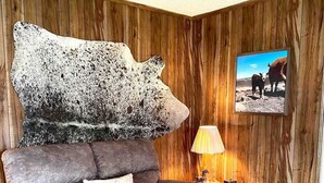Una sala de estar con un sofá marrón, una lámpara, una pared de madera y un cuadro con una vaca.