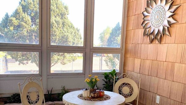 Decoración mural con diseño de sol, una mesa redonda con sillas y vistas amplias a través de grandes ventanales.