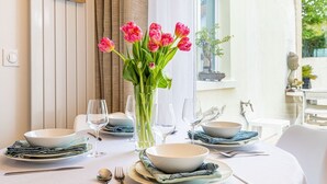 Ein Esstisch, gedeckt mit weißen Tellern, Schüsseln und Besteck, mit einer Vase voller pinkfarbener Tulpen.