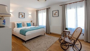 Ein modernes Schlafzimmer mit einem großen Bett, einem Schaukelstuhl und Blick ins Freie durch große Fenster.