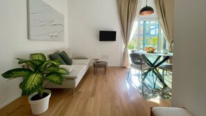 En moderne stue med sofa, en stueplante, et fjernsyn og et spiseområde med bord og stole.