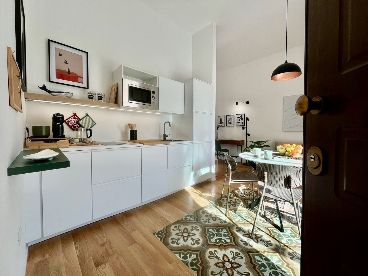 Et moderne køkken med hvide skabe, en mikrobølgeovn og en vask. Der er et spiseområde med et bord og stole, og en tæppe med et mønster på gulvet.