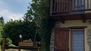 Un edificio rústico con un balcón de madera, una puerta grande de madera y un ventanal pequeño con celosía decorada.