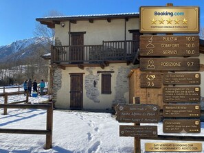 A mountain lodge with a wooden balcony, a signboard with ratings, and a snowy landscape.