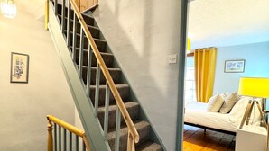 A staircase with wooden handrails leading to a bedroom with a bed, a bedside table, and a lamp. - The Cottage, 3 Bedroom, Pets Welcome (Ulverston)