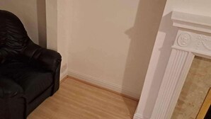 Una stanza con una poltrona in pelle nera, un caminetto bianco e pavimento in legno.