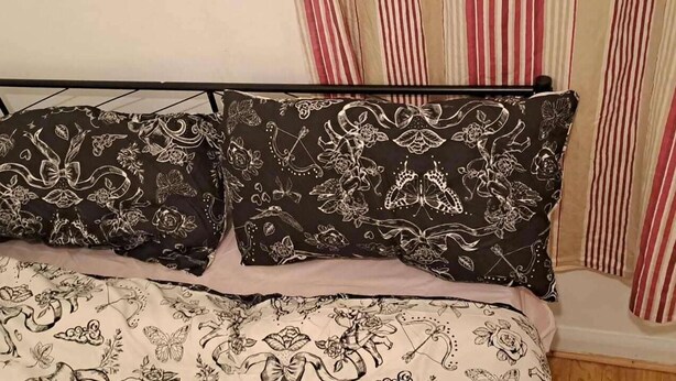 Un letto con una coperta a righe bianche e nere e due cuscini con un motivo floreale.