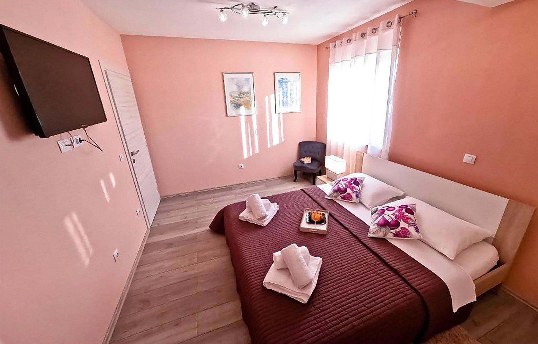 A hotel room with a large bed, a chair, a TV mounted on the wall, and two framed pictures on the wall.