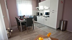 A modern kitchen with white cabinets, a dining table set for two, and a small breakfast table with orange slices. - Lovely apartment in Pula (Pula)