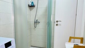 Ett badrum med en dusch som är avskärmad med glasväggar, en vit dörr och en tvättmaskin.