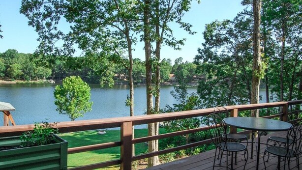 A wooden deck with a table and chairs overlooking a lake, surrounded by trees.