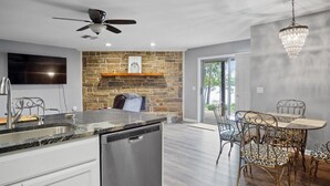 A modern kitchen with a stone backsplash, a dishwasher, a dining area with a table and chairs, and a chandelier.