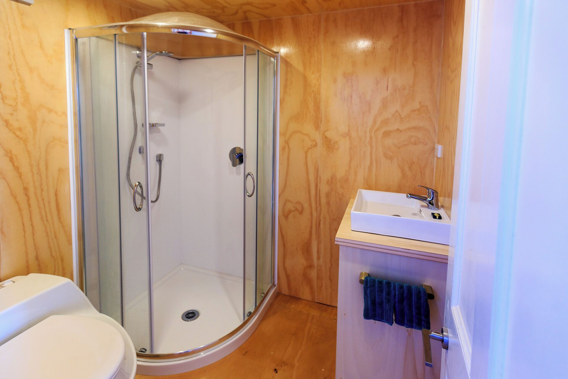 Un baño moderno con ducha de vidrio, lavamanos blanco y tocador de madera.