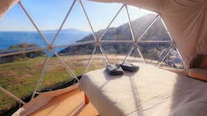 A bed with a view of a mountainous landscape through a tent-like structure. - Escarpment Domes (Porirua)