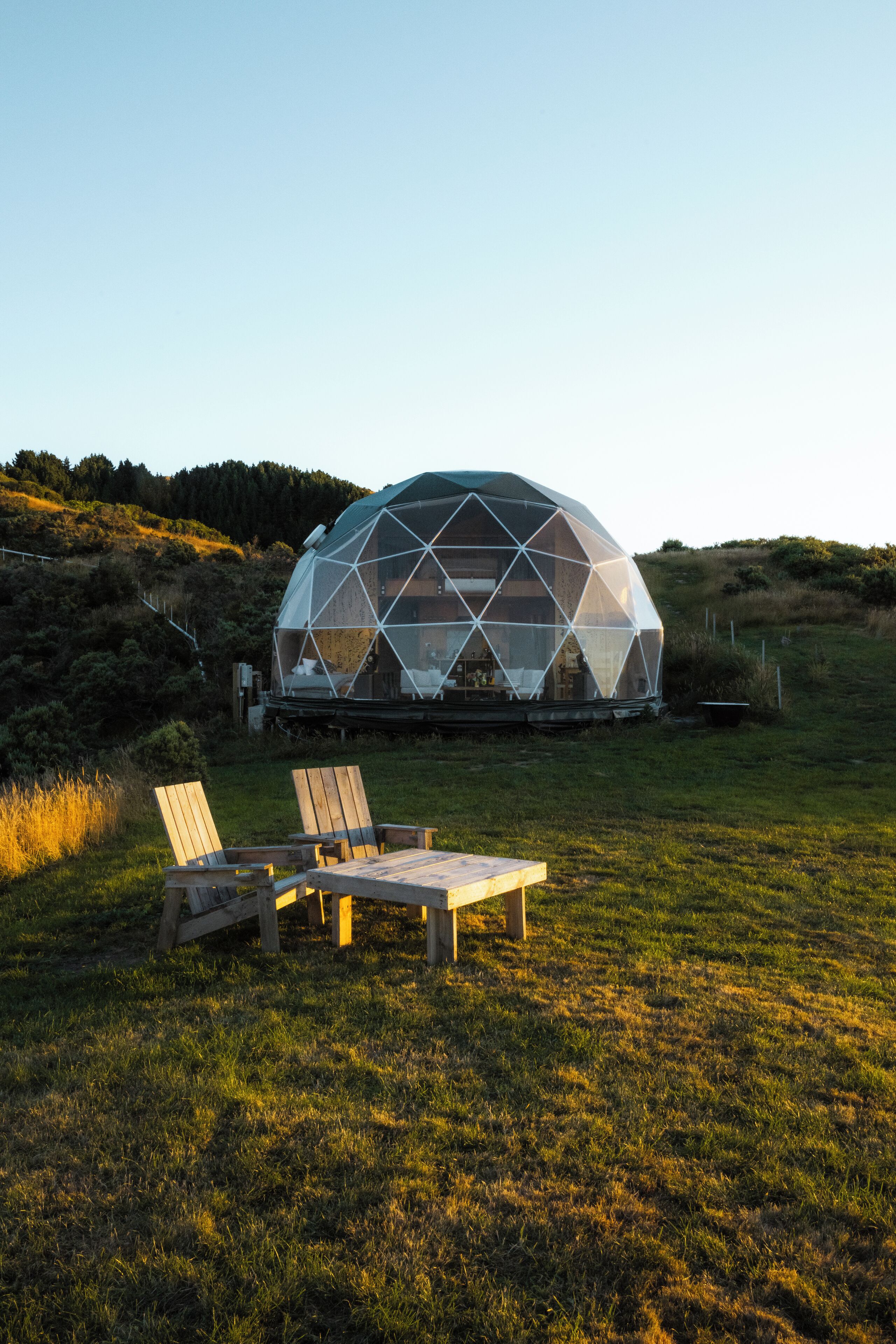 Estructura en forma de cúpula geodésica con una terraza de madera y sillas al frente.