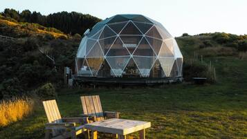 Estructura en forma de cúpula geodésica con una terraza de madera y sillas al frente.