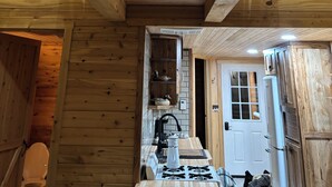 Un intérieur en bois avec un plafond en pente, un coin cuisine équipé d’une cuisinière et une porte donnant sur une autre pièce.