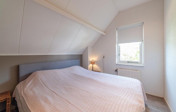 A bedroom with a sloped ceiling, a bed, a nightstand, a lamp, and a window.