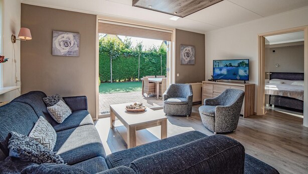 A modern living room with a sofa, armchairs, a coffee table, and a TV. There is a garden visible through the glass door. - Beautiful home in Wemeldinge with sauna (Wemeldinge)