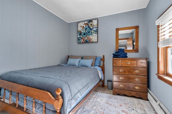 A bedroom with a bed, dresser, mirror, and artwork on the wall. - Cove Cottage | Close To Newport & Beaches (Portsmouth)