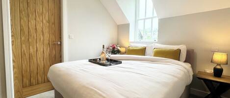 A bedroom with a large bed, a wooden door, a nightstand with a lamp, and a window with natural light.