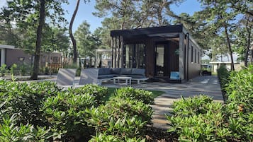 A modern outdoor seating area with a built-in sofa and chairs, surrounded by lush greenery and trees.