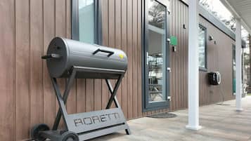 A modern building with a wooden exterior, a large window, and a barbecue grill labeled "BORETTI" on wheels.