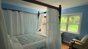 Un dormitorio con cama con dosel, una ventana con vistas a la vegetación y una silla.