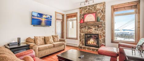 A living room with a stone fireplace, a sofa, a coffee table, and a television mounted on the wall.