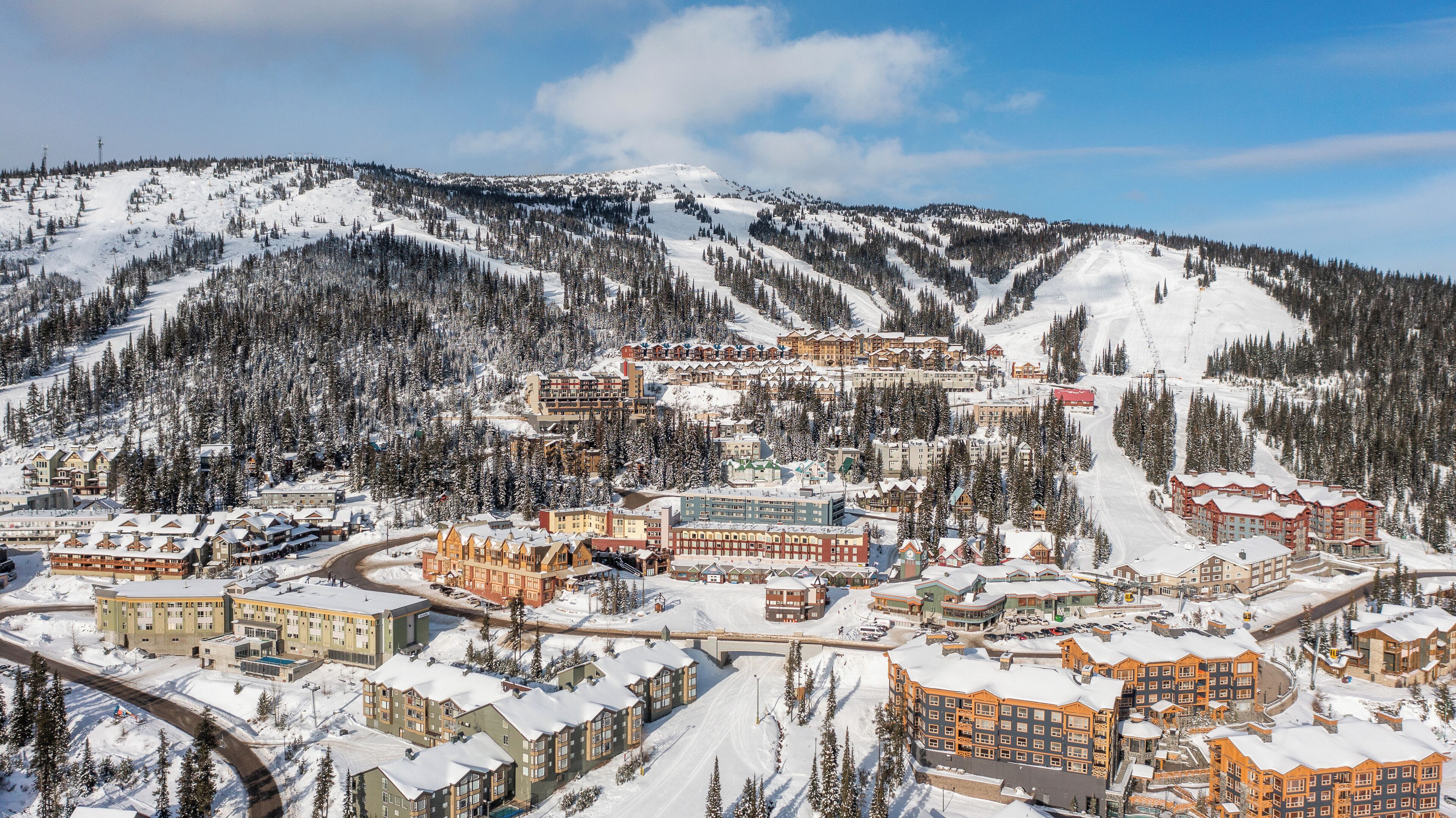 A snow-covered mountain town with a variety of buildings, including hotels and apartments, surrounded by dense forests and snow-covered slopes.