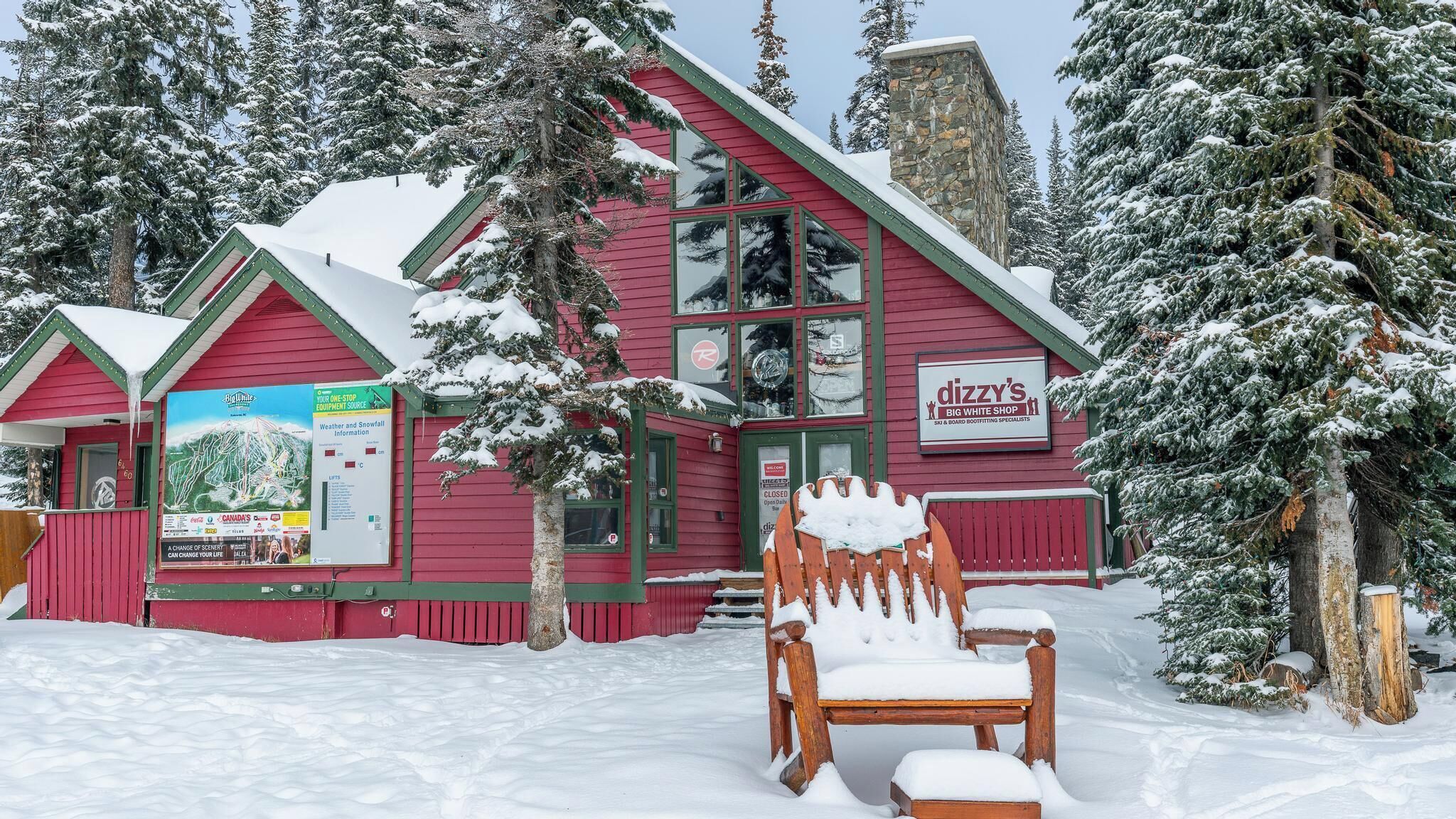 Ein rotes Gebäude mit einem Schild für 'Dizzy's Big White Shop' und einem mit Schnee bedeckten Stuhl davor.