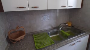 Een keuken met witte kastjes, een granieten aanrecht, een spoelbak, een groen snijplankje en een rieten mand.