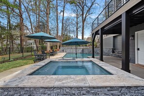 A swimming pool with stone walls, two umbrellas, and a patio area with chairs and a table.