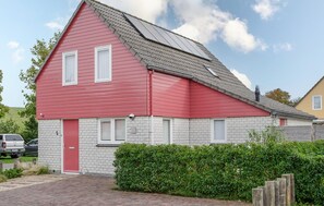 Stunning two-story house with a brick foundation and a red door, set amidst a well-manicured hedge and paved driveway.