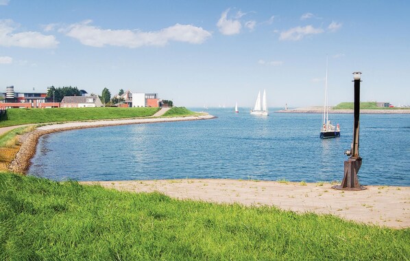 A waterfront scene with a grassy path, a sailboat, and buildings in the background. - Stunning home in Wemeldinge with sauna (Wemeldinge)