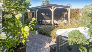 A covered outdoor seating area with a wooden pergola, a brick pathway, and potted plants. - Stunning home in Wemeldinge with sauna (Wemeldinge)