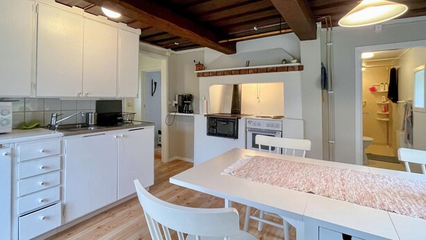 Een kleine keuken met witte kastjes, een houten vloer en een centraal eiland met stoelen.